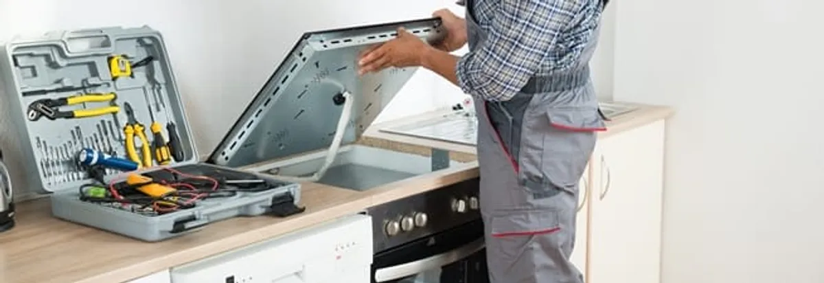 Cooktop repair technician lifting a built-in stovetop for service in San Antonio, TX