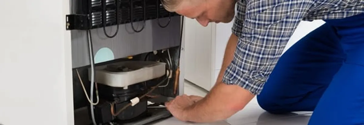 Refrigerator repair technician servicing the compressor and condenser area in San Antonio, TX